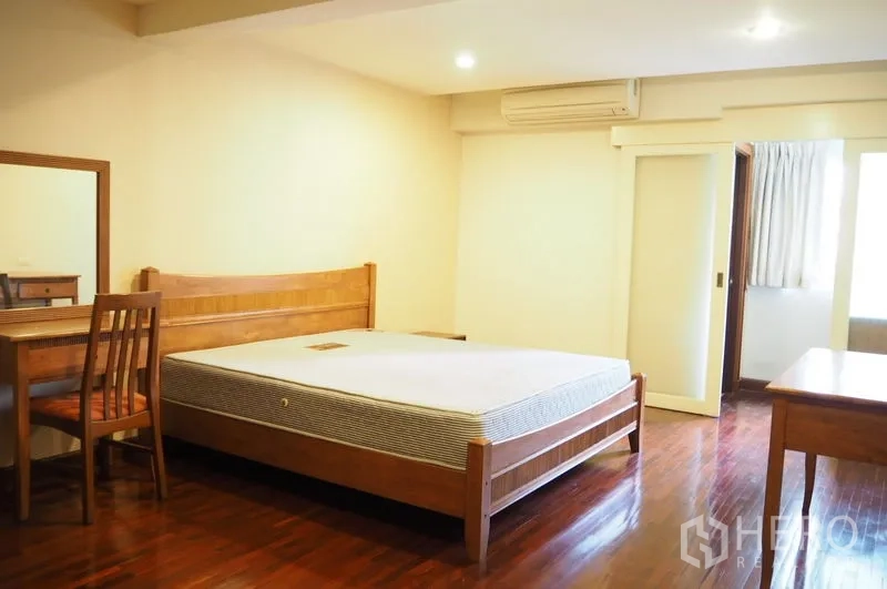 Condominium for rent in Pathum Wan, Bangkok - Spacious bedroom with wooden bed, desk and door to ensuite bathroom