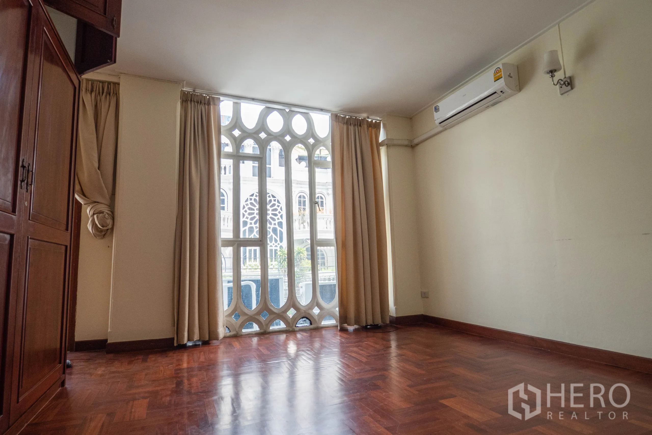 Townhouse for rent in Khlong Toei, Bangkok - Bright room with parquet flooring, a large arched lattice window, air conditioner and built-in wooden cabinet.