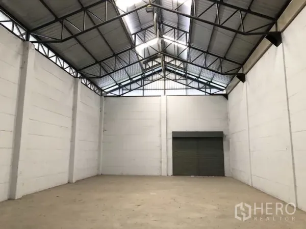 Warehouse for rent in Lat Lum Kaeo, Pathum Thani - Empty warehouse interior with a high gable steel roof and a large roller shutter door.