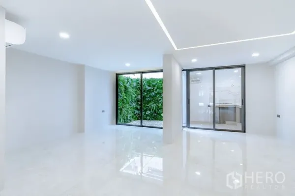 Townhouse for sale - Bright open-plan living area with glossy floors and sliding doors facing a lush green privacy wall.