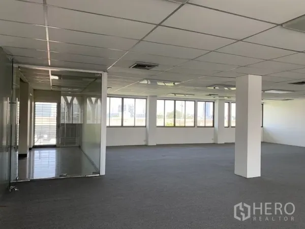 Office Space for rent in Bang Kapi, Bangkok - Expansive office space with support columns, suspended ceiling lighting, and an adjacent glass-walled room beside wide windows.
