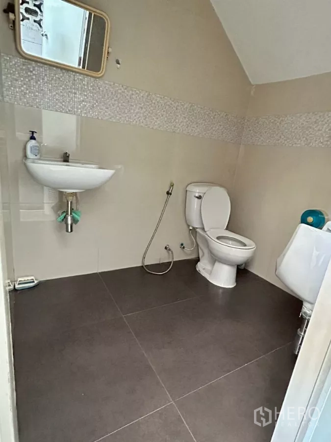 Warehouse for rent in Suan Luang, Bangkok - Clean restroom with toilet, urinal, wall‑mounted sink and tiled finishes.