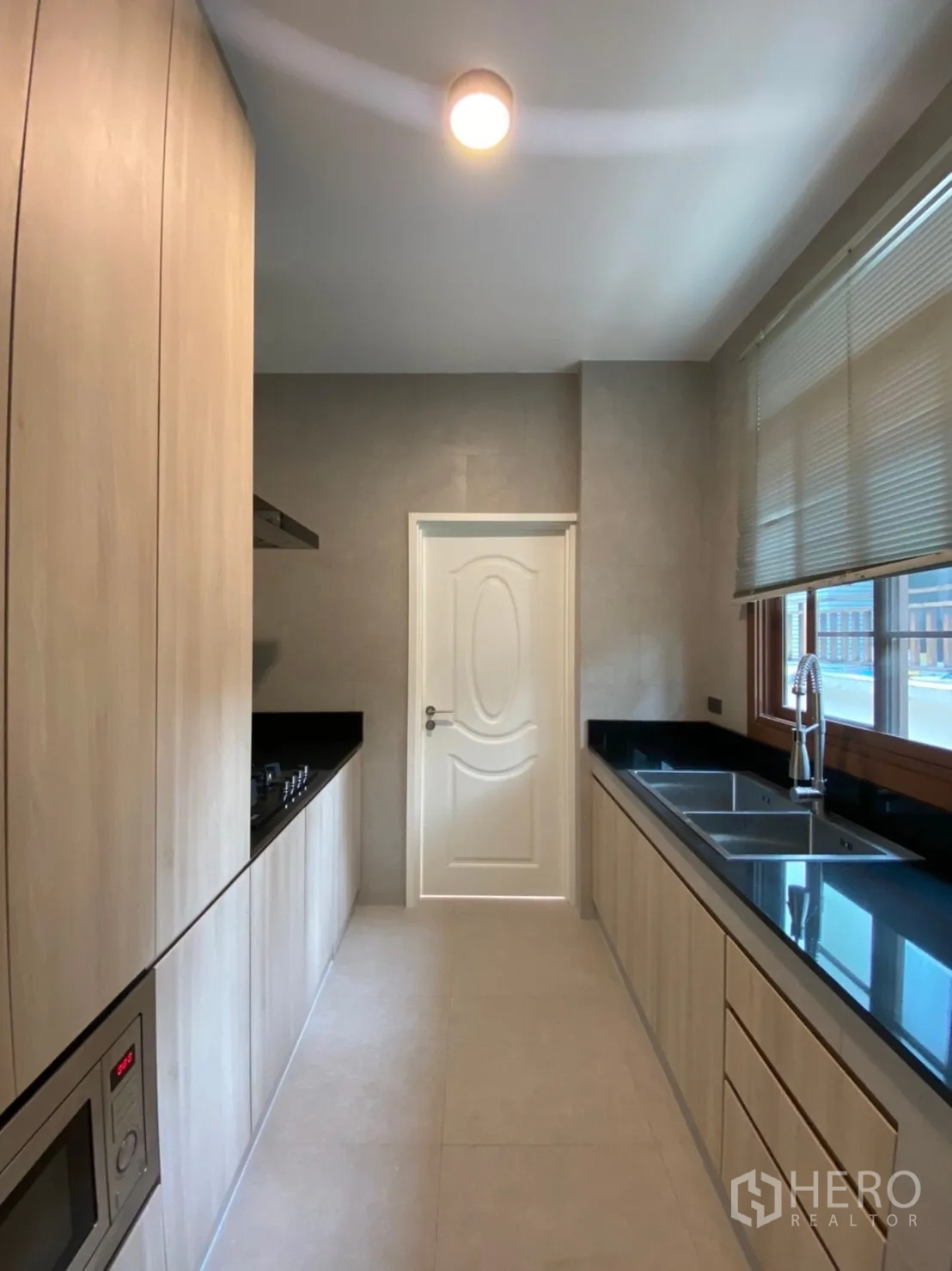 Detached House for rent in Bang Phli, Samut Prakan - Separate Thai kitchen with long black countertops, gas hob, double sink and wood cabinetry.