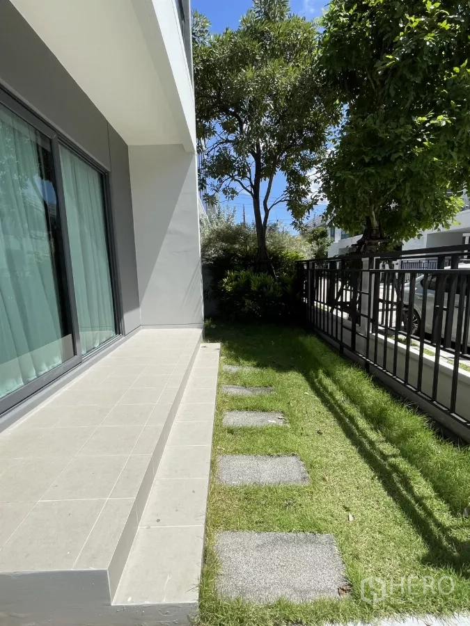 Detached House for rent in Bang Phli, Samut Prakan - Side garden with stepping stones beside sliding doors and metal fence.