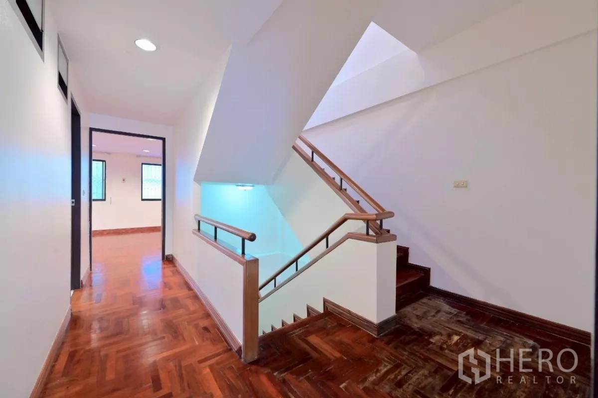Townhouse for sale in Watthana, Bangkok - Upper-floor landing with polished wood floors, stairwell, and bedroom doors.