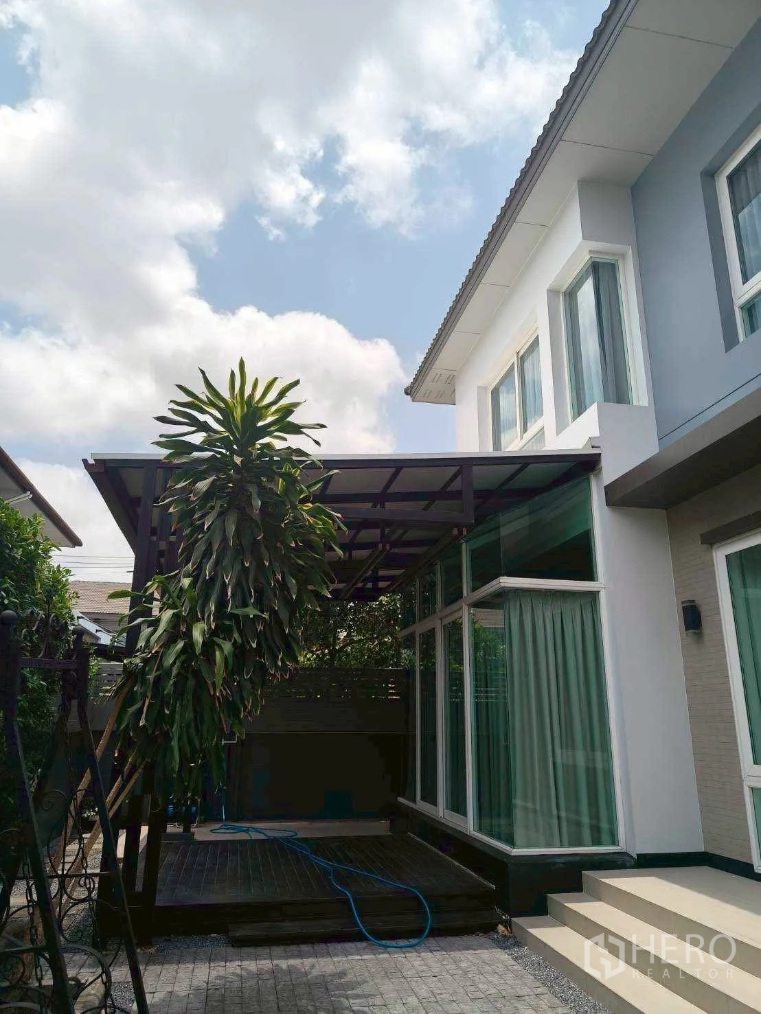 Detached House for rent or sale in Bang Phli, Samut Prakan - Exterior side of the house with a covered terrace structure and tall greenery.