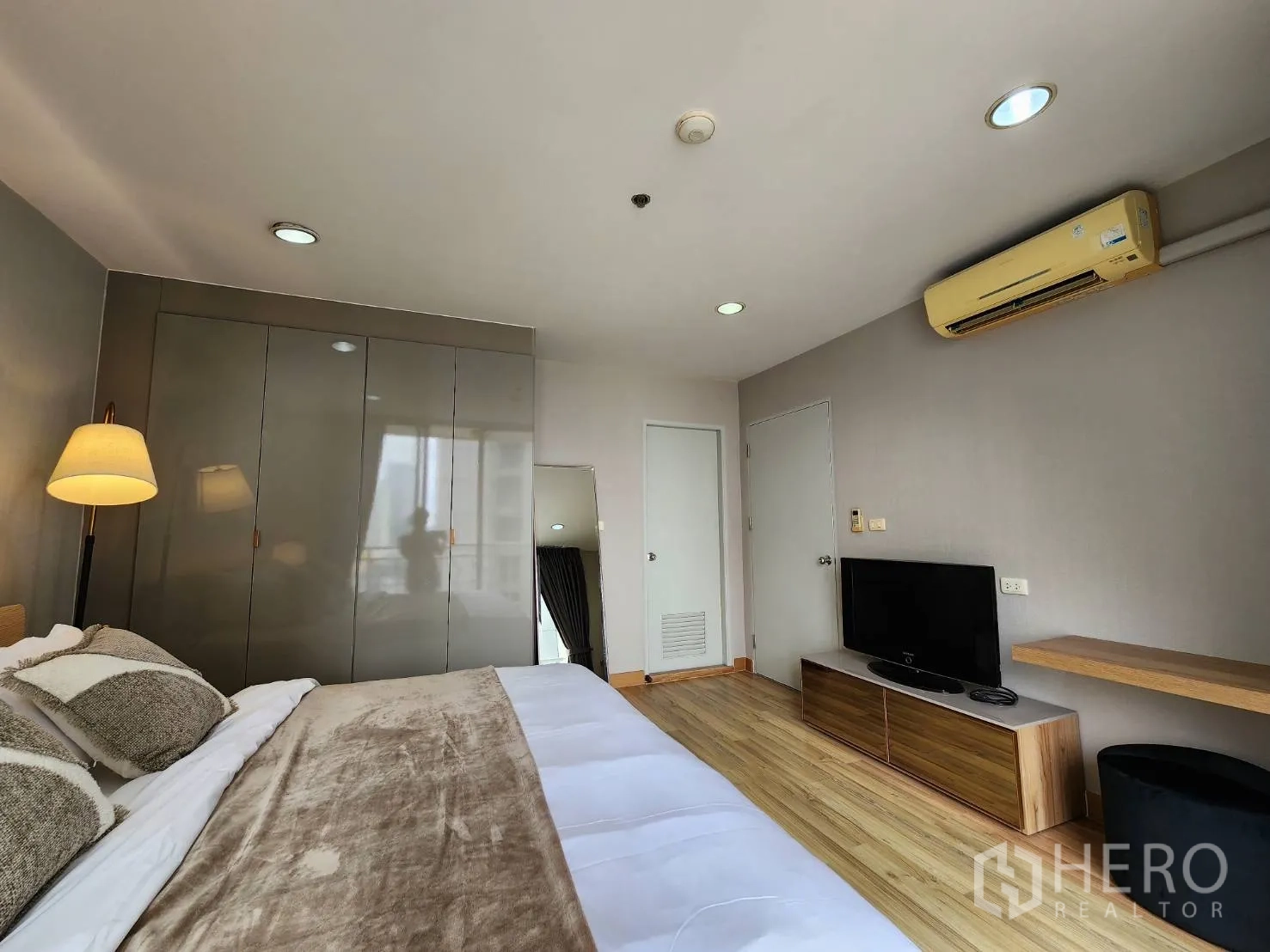 Condominium for rent in Watthana, Bangkok - Bedroom with TV console, air conditioner and tall wardrobe on wood floors.