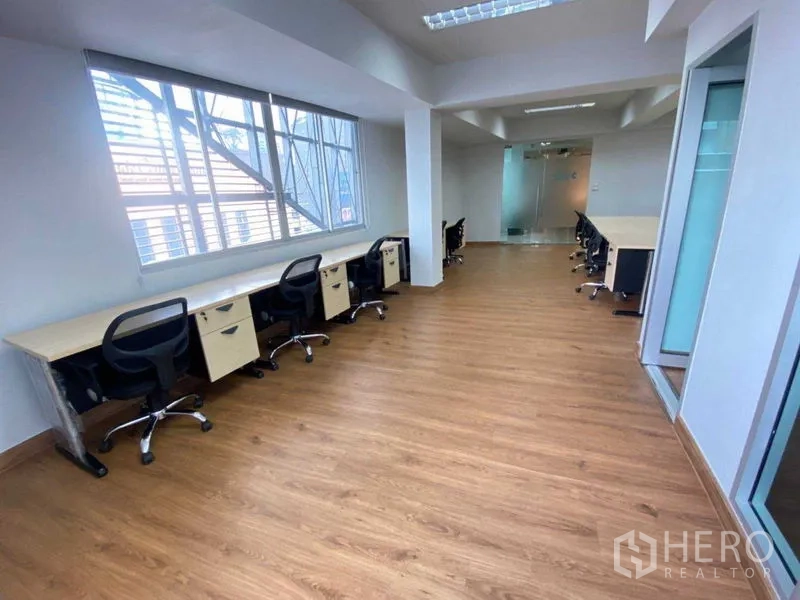 Office Space for rent in Khlong Toei, Bangkok - Corridor-style workstation zone with desks along a large window and a glass entry door.