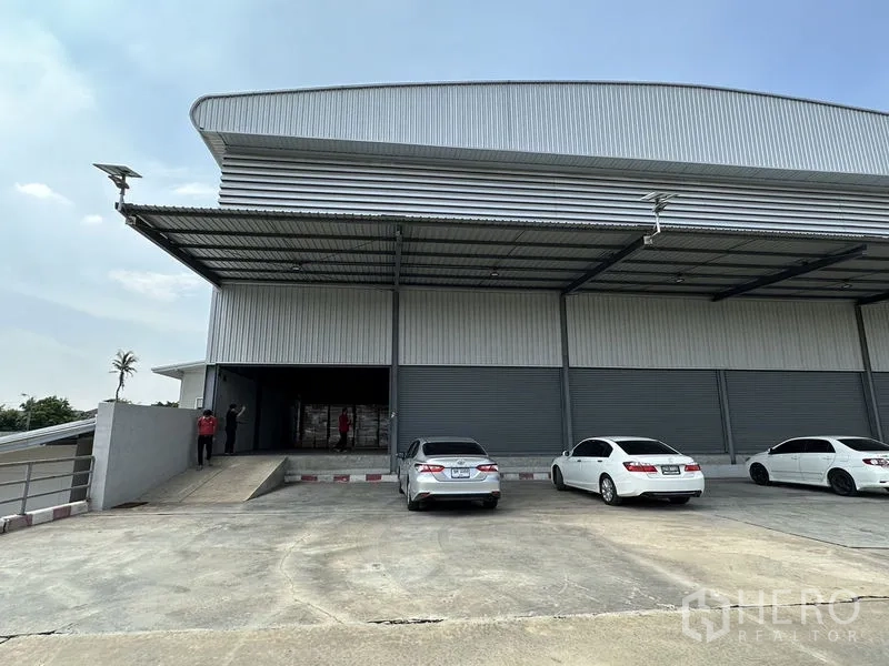 Warehouse for rent in Lat Krabang, Bangkok - Front facade with several roller shutters, a covered loading area and ramp access with parking.