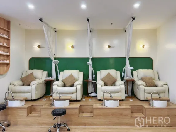 零售空间 出租 - 美甲店足疗区，四张米色躺椅配独立足浴盆，绿色背景墙与暖光灯。