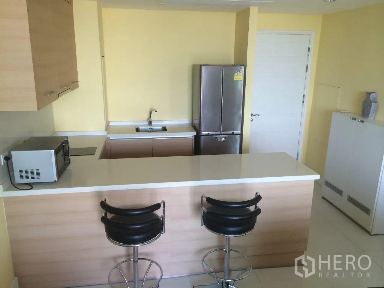 公寓 出租在Khlong Toei, Bangkok - 浅木色开放式厨房吧台，吧椅与不锈钢冰箱。