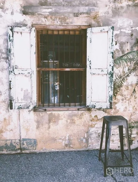 Shophouse for rent in Bang Rak, Bangkok - Close-up of barred window with peeling white shutters and a metal stool.