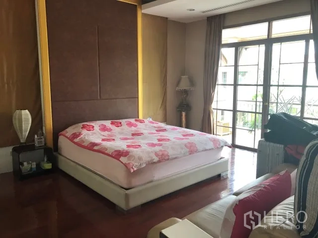Detached House for rent in Bang Phli, Samut Prakan - Master bedroom with wood floors, feature wall and sliding glass doors opening to a balcony.
