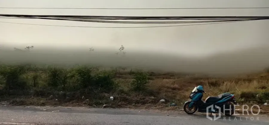 Land for sale in Wang Noi, Phra Nakhon Si Ayutthaya - Roadside vacant land with tall grass, overhead power lines, and a parked scooter in Wang Noi, Phra Nakhon Si Ayutthaya.