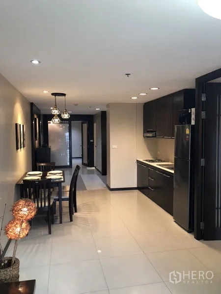 Condominium for rent in Khlong Toei, Bangkok - Open-plan kitchen with dark cabinets, refrigerator and adjoining dining area.