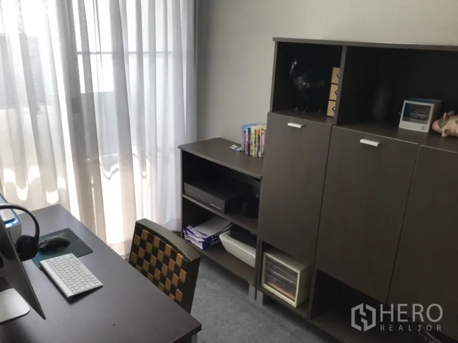Condominium for rent in Watthana, Bangkok - Bright home office with desk, computer and dark wood storage beside sheer balcony curtains.