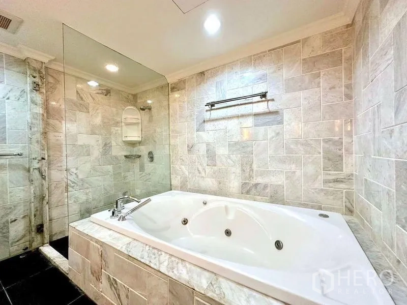 Condominium for rent - Marble-tiled bathroom with Jacuzzi bathtub and glass-enclosed shower.