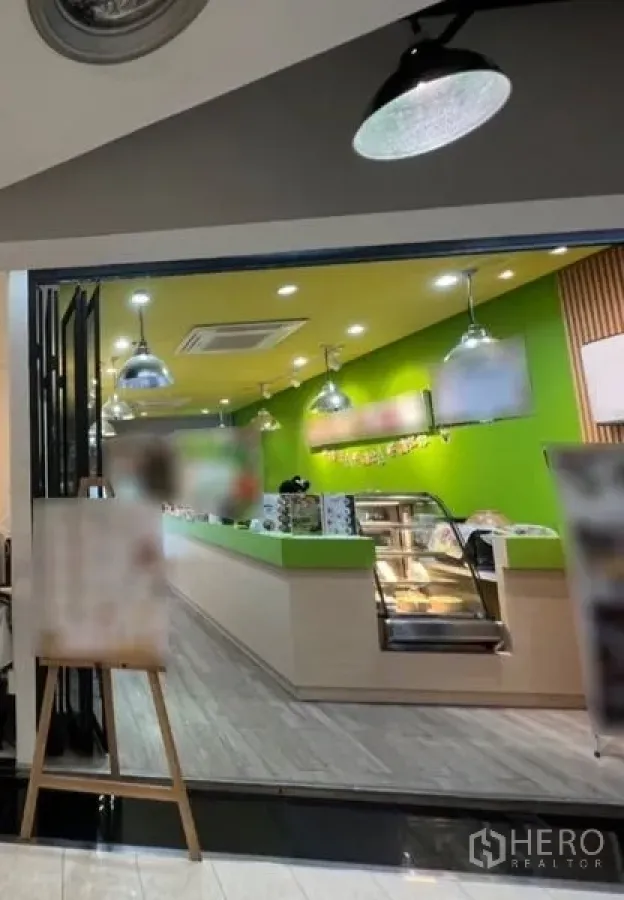 零售空间 出租在Watthana, Bangkok - 玻璃门面零售店内景，绿色强调墙、吊灯、木纹地板，配服务吧台与展示柜。