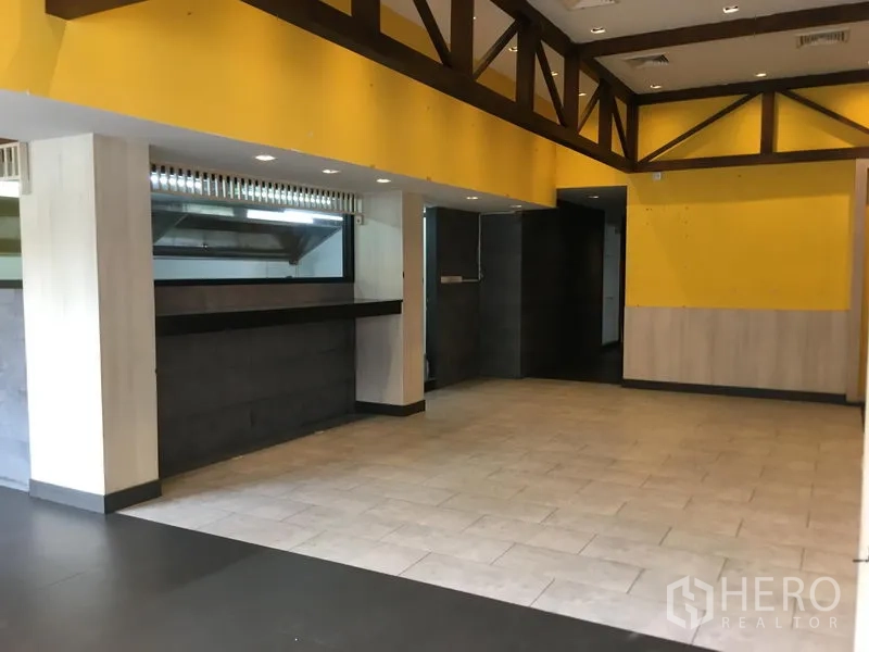 零售空间 出租在Khlong Toei, Bangkok - 开放式店内空间，黄色特色墙、木梁、地砖与长服务台。