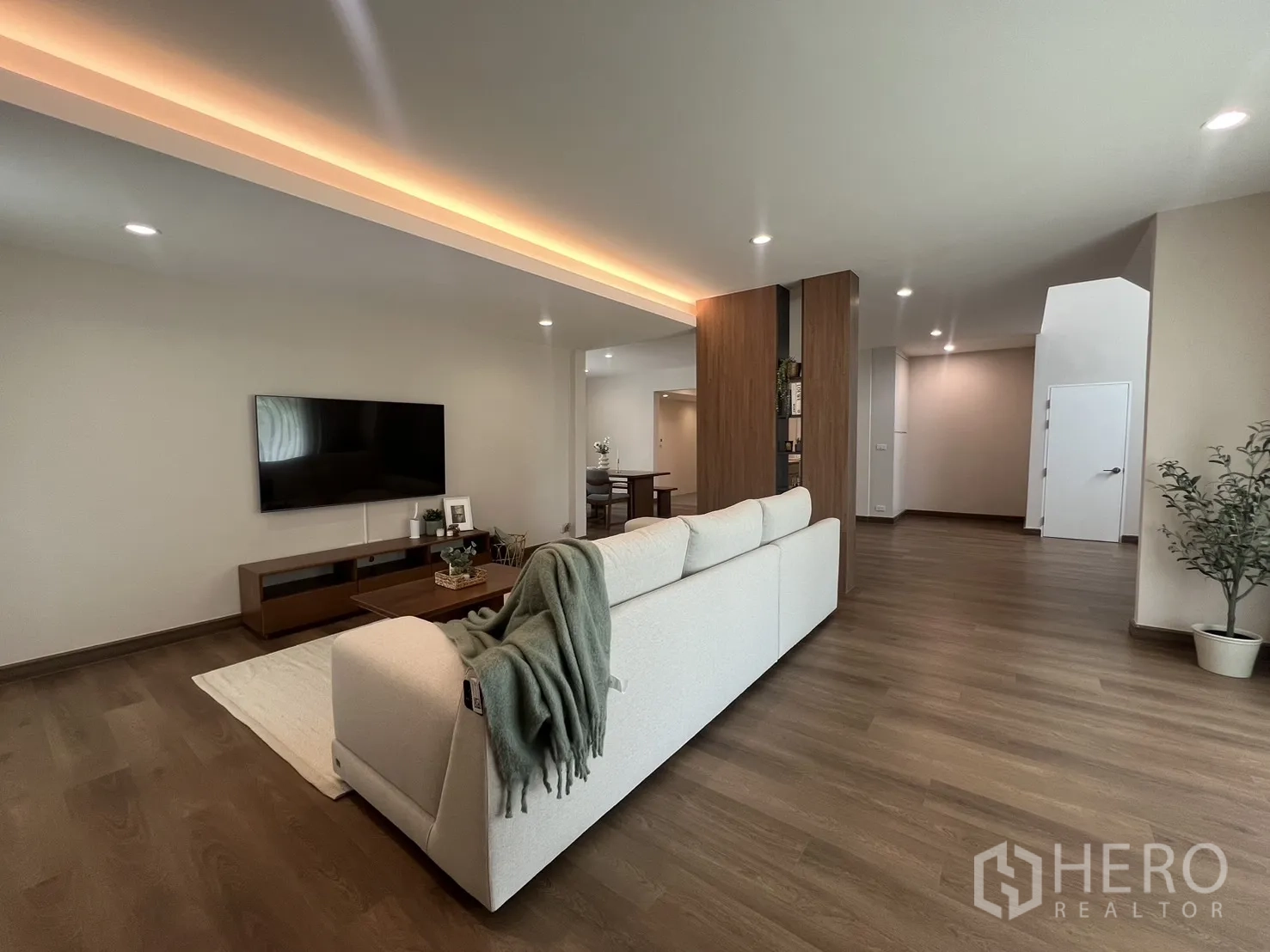 独立式住宅 出租在Mueang Samut Prakan, Samut Prakan - 明亮客厅，L 形沙发、电视墙与木地板。