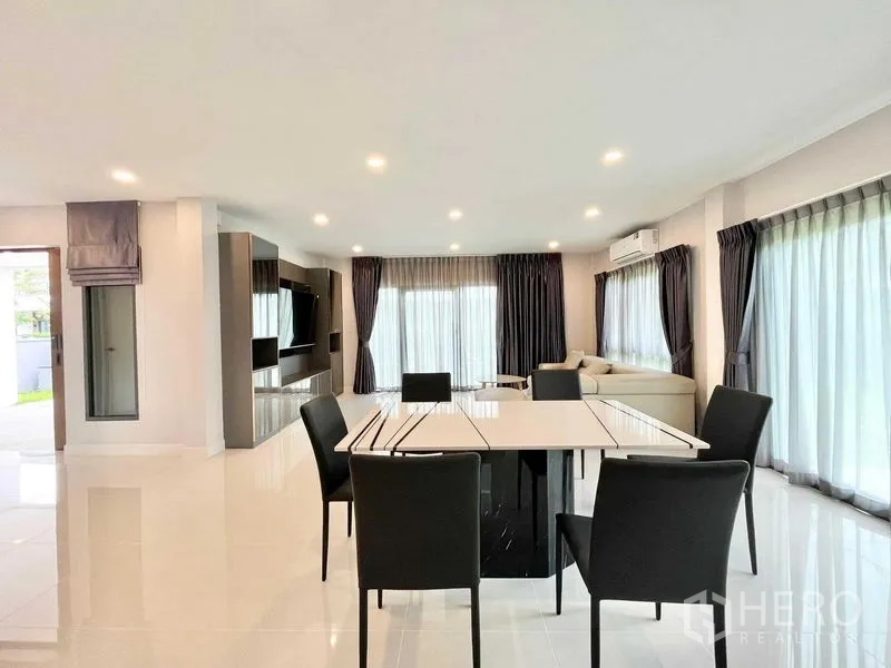 Detached House for rent in Don Mueang, Bangkok - Dining area facing a TV wall and glass doors that open to the patio and greenery.