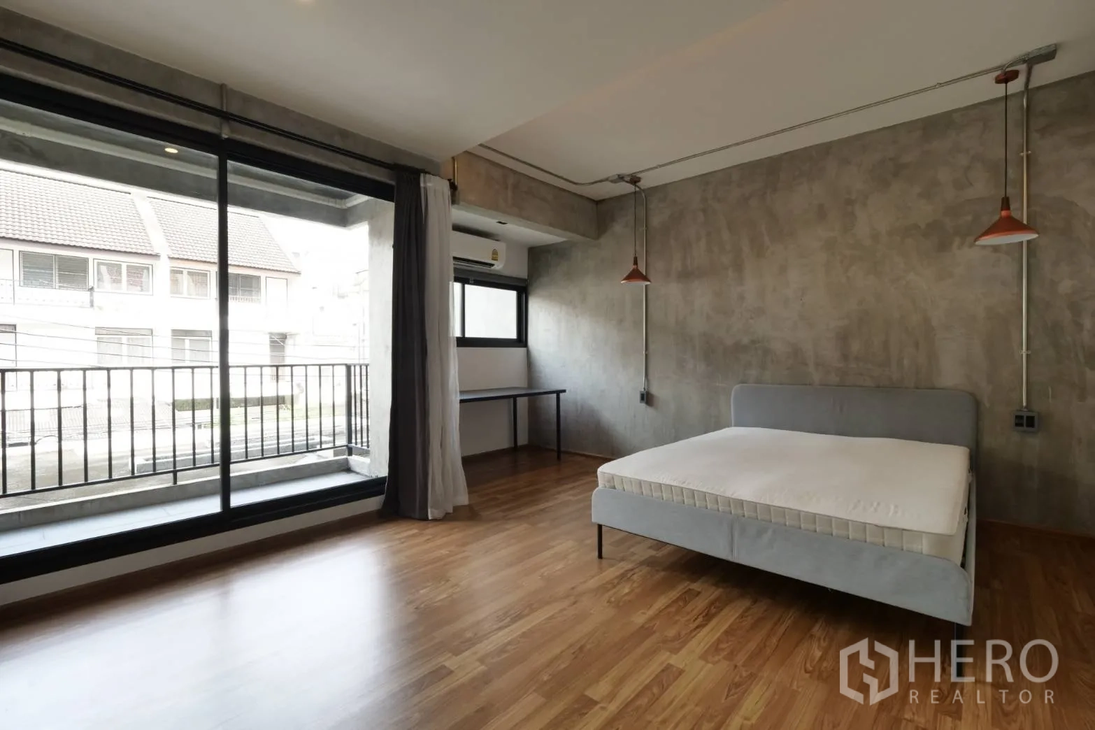 Townhouse for rent in Khlong Toei, Bangkok - Large bedroom with balcony access, concrete feature wall and wood floors.