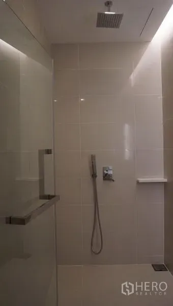 Condominium for rent in Bang Sue, Bangkok - Tiled bathroom featuring a glass shower enclosure with rainfall showerhead and handheld spray.