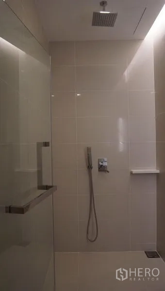 Condominium for rent in Bang Sue, Bangkok - Tiled bathroom featuring a glass shower enclosure with rainfall showerhead and handheld spray.