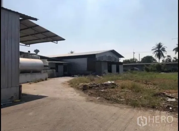 Factory for rent in Bang Khla, Chachoengsao - Open concrete yard with metal sheds, a storage tank and greenery around the industrial site.