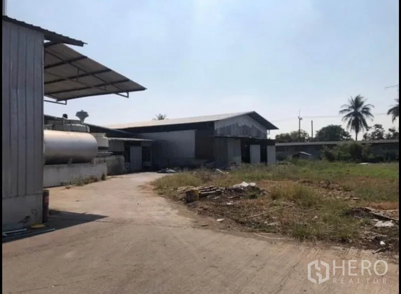 Factory for rent in Bang Khla, Chachoengsao - Open concrete yard with metal sheds, a storage tank and greenery around the industrial site.