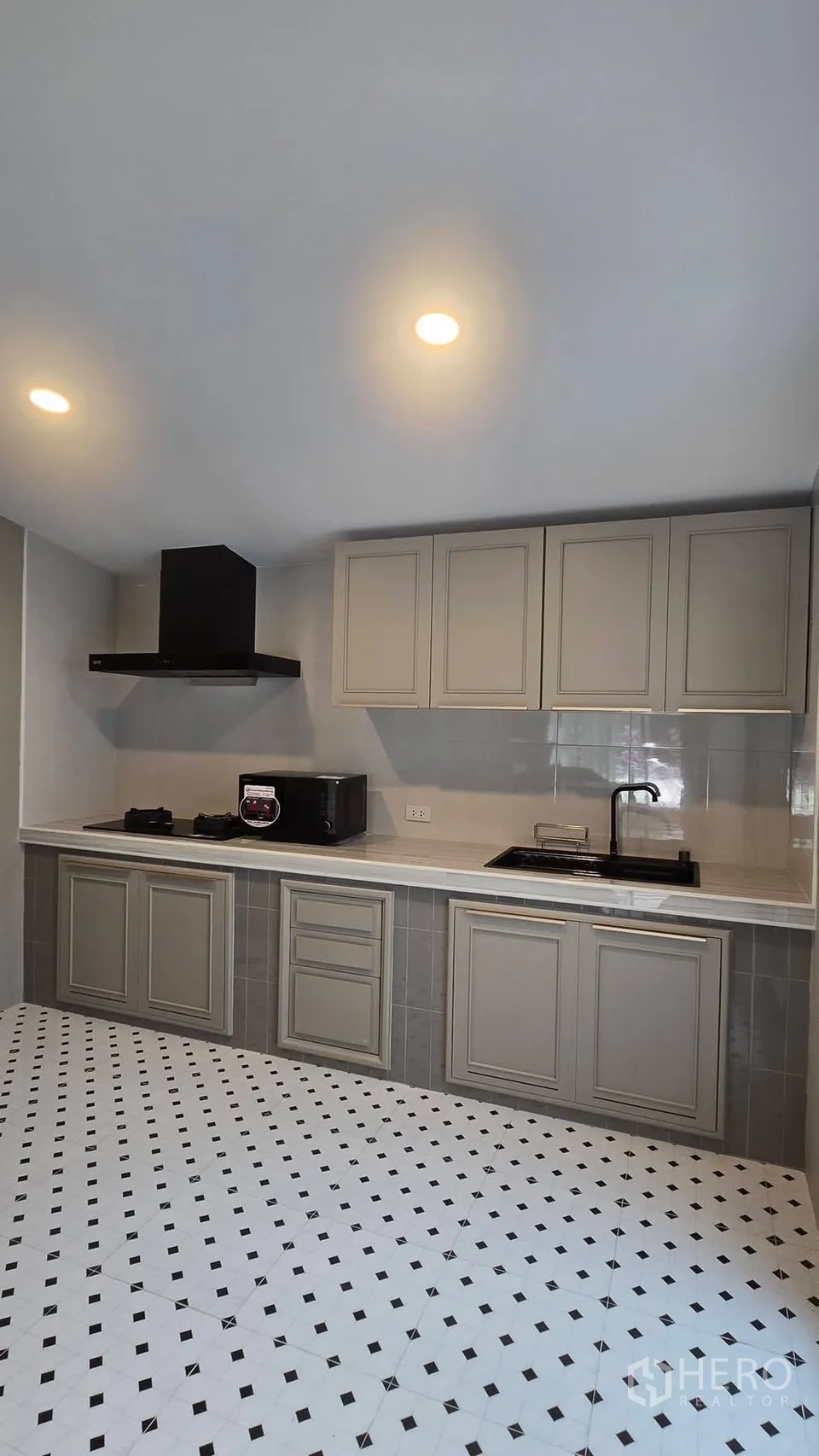 Townhouse for rent in Bang Phli, Samut Prakan - Fully fitted kitchen with grey cabinetry, gas hob, hood, and patterned floor tiles.