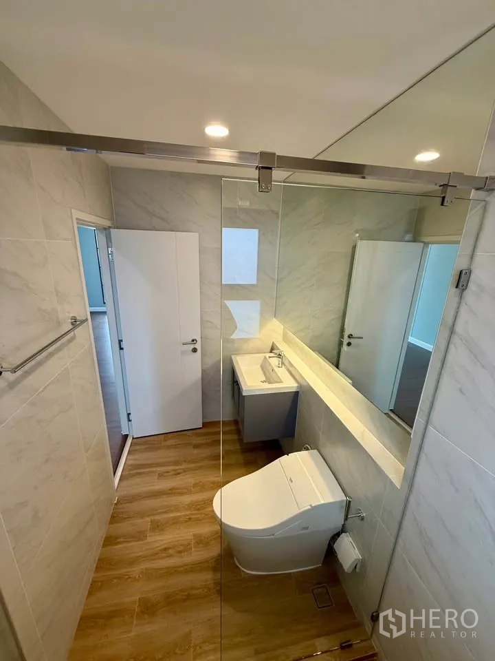 Detached House for rent in Don Mueang, Bangkok - Bathroom with glass shower screen, long mirror, and wood-look floor.