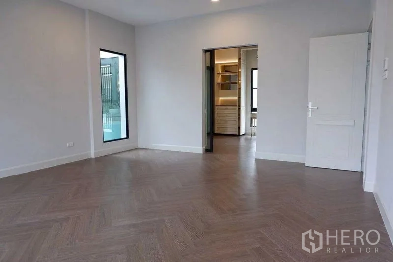 Detached House for sale in Saphan Sung, Bangkok - Empty bedroom with herringbone wood floor and doorway to a walk-in closet.