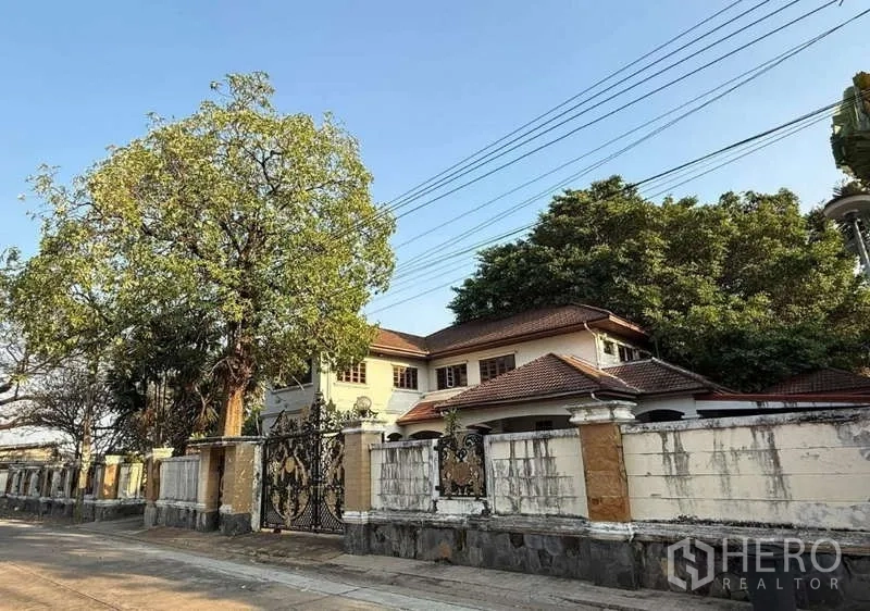 บ้าน ขายในSai Mai, Bangkok - บ้านเดี่ยวสองชั้น สายไหม กรุงเทพฯ หลังคากระเบื้อง รั้วสูง ประตูเหล็กดัดลายหรู และต้นไม้ใหญ่ริมถนนสงบ