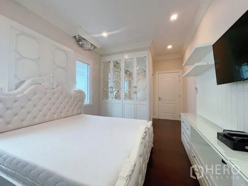 Detached House for rent or sale in Bang Phli, Samut Prakan - Bedroom with white tufted headboard, mirrored wardrobe, wall‑mounted TV, and built‑ins.