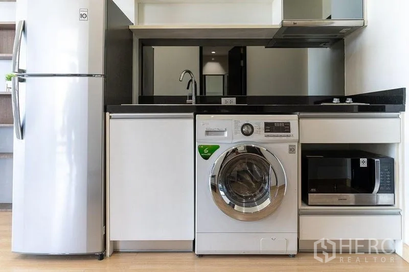 Condominium for rent - Straight-on view of kitchen with refrigerator, washing machine, microwave and stovetop.