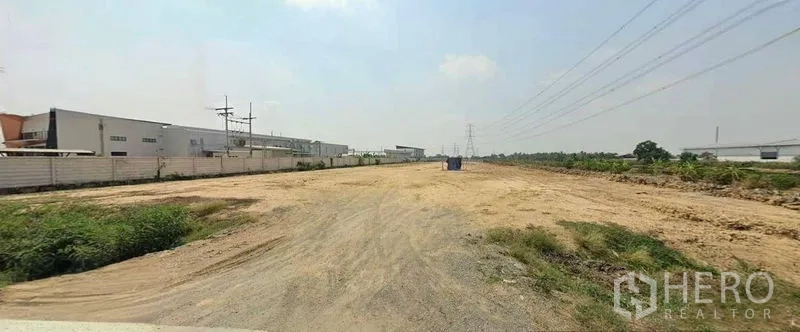 Land for sale in Sai Noi, Nonthaburi - Expansive graded land ready for development, flanked by factory blocks and utility lines.