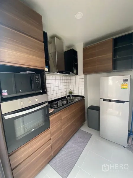 Detached House for rent in Bang Phli, Samut Prakan - Compact modern kitchen with wood cabinetry, gas hob, oven, range hood and refrigerator.