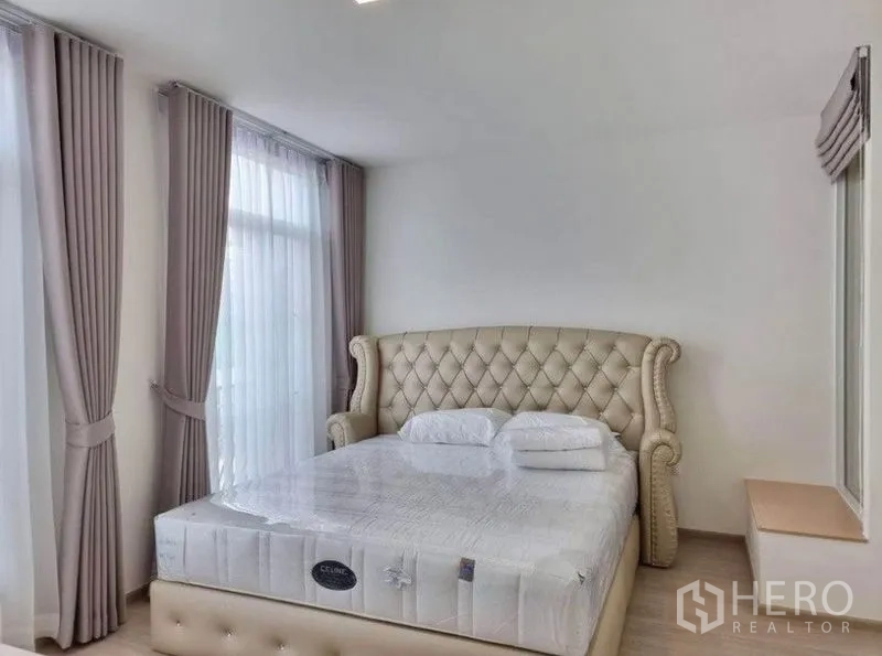 联排别墅 出租在Prawet, Bangkok - 主卧配软包床头，转角大窗与纱帘，浅色木地板。