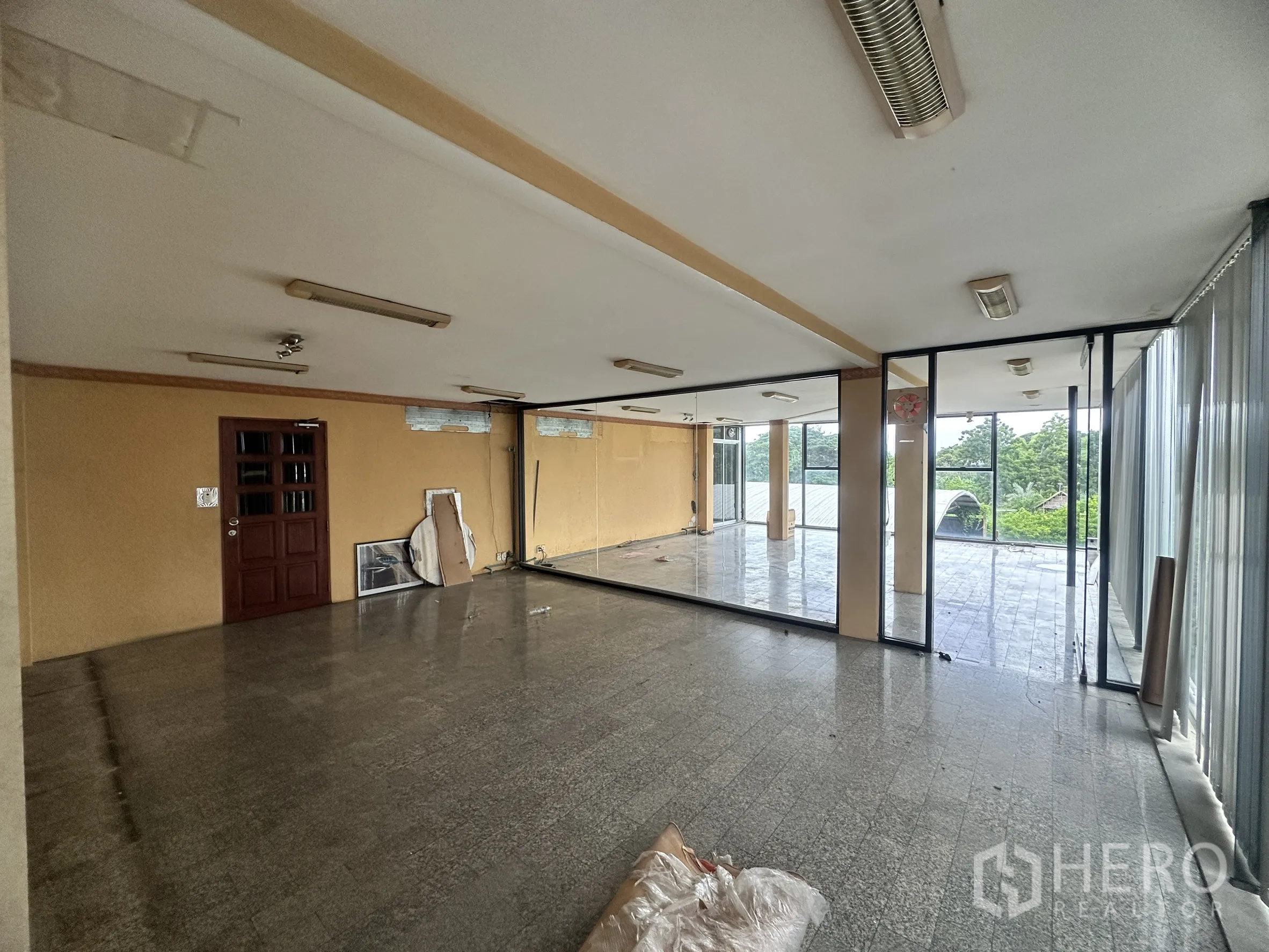 Factory for sale in Bang Bua Thong, Nonthaburi - Empty office room with glass walls, fluorescent lighting, and views of greenery.