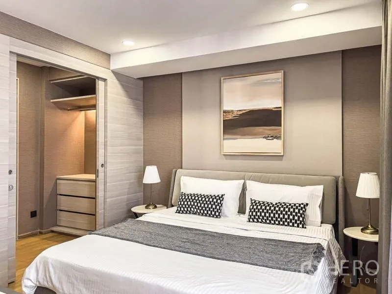 Condominium for rent in Pathum Wan, Bangkok - Bedroom with walk-in closet entrance and king bed flanked by bedside lamps.