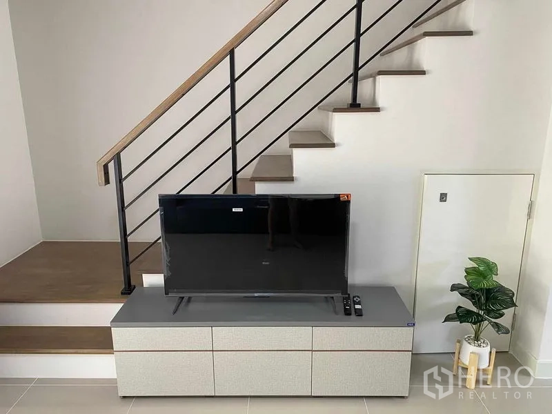 联排别墅 出租在Prawet, Bangkok - 楼梯下方电视柜，平板电视与室内绿植。