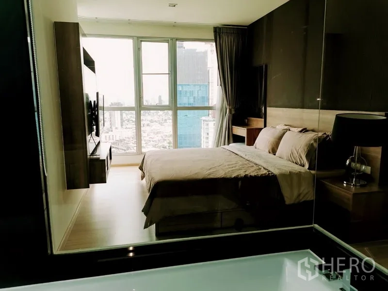 Condominium for rent in Khlong Toei, Bangkok - Master bedroom with floor-to-ceiling windows, city skyline view and wall-mounted TV.