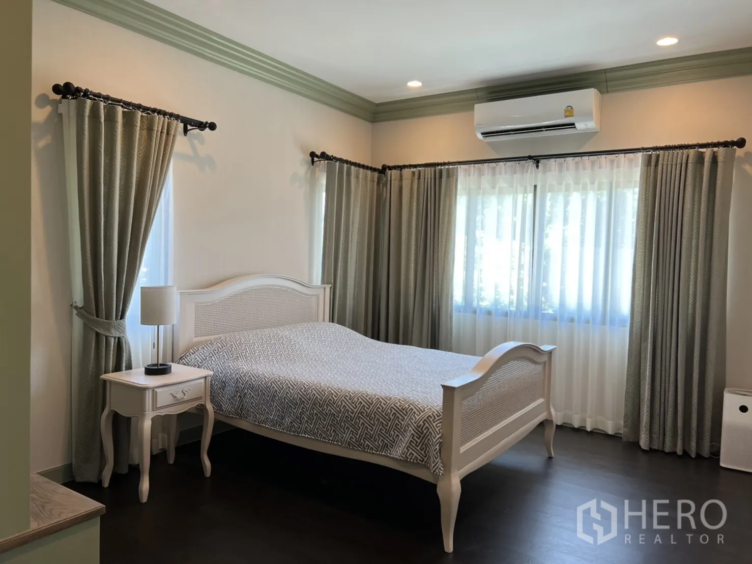Detached House for rent or sale in Bang Kapi, Bangkok - Sunlit bedroom with a white bed, bedside table and double-aspect windows dressed with curtains.