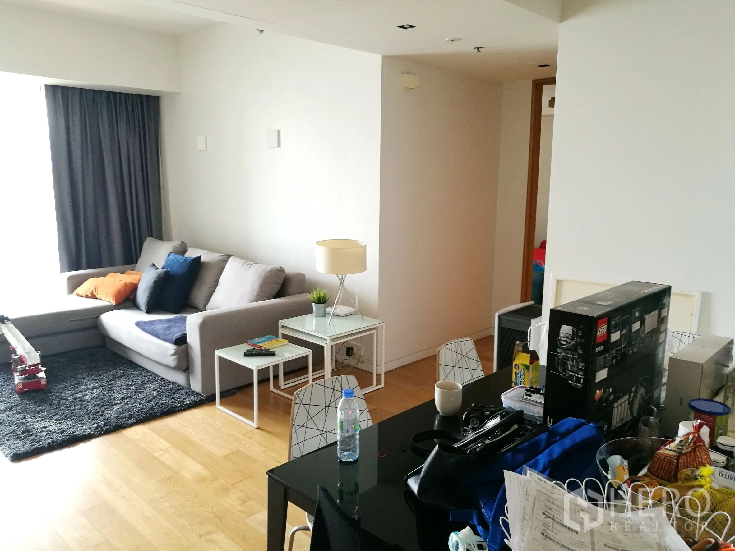 Condominium for rent or sale in Sathon, Bangkok - Open-plan living and dining space with sofa, dining table and large window with curtains.