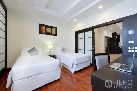 Apartment for rent in Watthana, Bangkok - Twin bedroom with two single beds, desk, and sliding doors on polished wood floors.