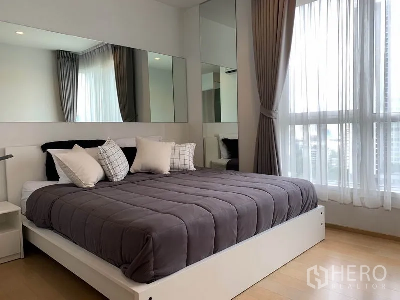 Condominium for rent in Watthana, Bangkok - Bedroom with large bed, mirrored headboard wall, and tall windows offering city views.
