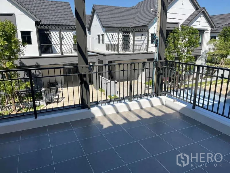 Detached House for rent in Bang Phli, Samut Prakan - Shaded upstairs balcony with gray tiles overlooking a modern housing estate and greenery.