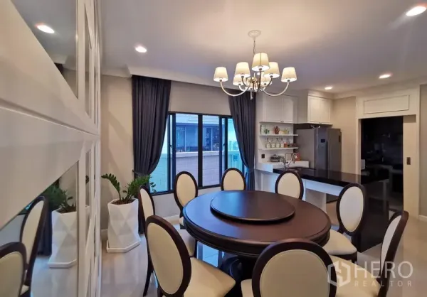 Detached House for rent or sale in Bang Kapi, Bangkok - Bright dining space with round table and chandelier beside a sleek kitchen and large sliding windows.