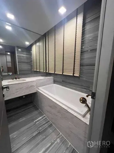 คอนโด ให้เช่าในWatthana, Bangkok - ห้องน้ำพร้อมอ่างอาบน้ำ เคาน์เตอร์ลายหินอ่อน และหน้าต่างติดมู่ลี่ โทนผนังสีเทาลายหิน